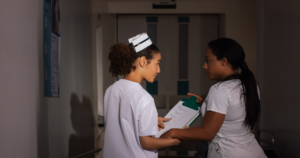 Image of 2 nurses standing, discussing a case in a low lit room. The Weekend Shift