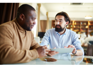 Image of 2 men talking at a desk. Honest conversations at work