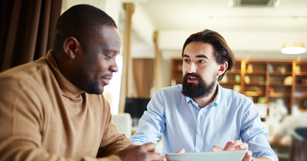 Image of 2 men talking at a desk. Why Honest Conversations Feel Risky When Power Isn’t Equal at Work