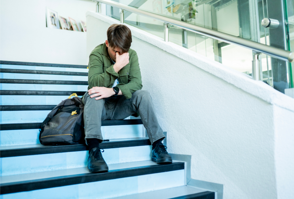 Image of boy with his backpack beside him on schools steps with his head down. Academic Struggles