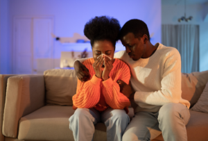 Image of a woman crying while a man sits beside her hugging her. Broken trust