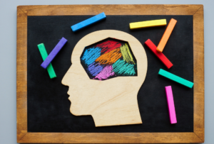 Image of a silhouette of a man's head on a chalboard with different areas of the brain colored with chalk. Neurodiversity