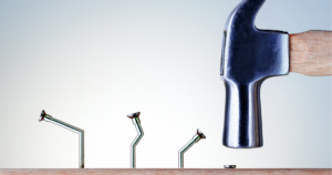 Image of hammer hitting a nail and other bent nails that it previously tried to hit in the board but failed. Stop Asking Why the Person Failed. Human Factors