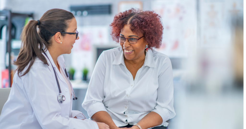 Image is a patient sitting with doctor, both smiling as the doctor speaks to her. From Compliance to Partnership